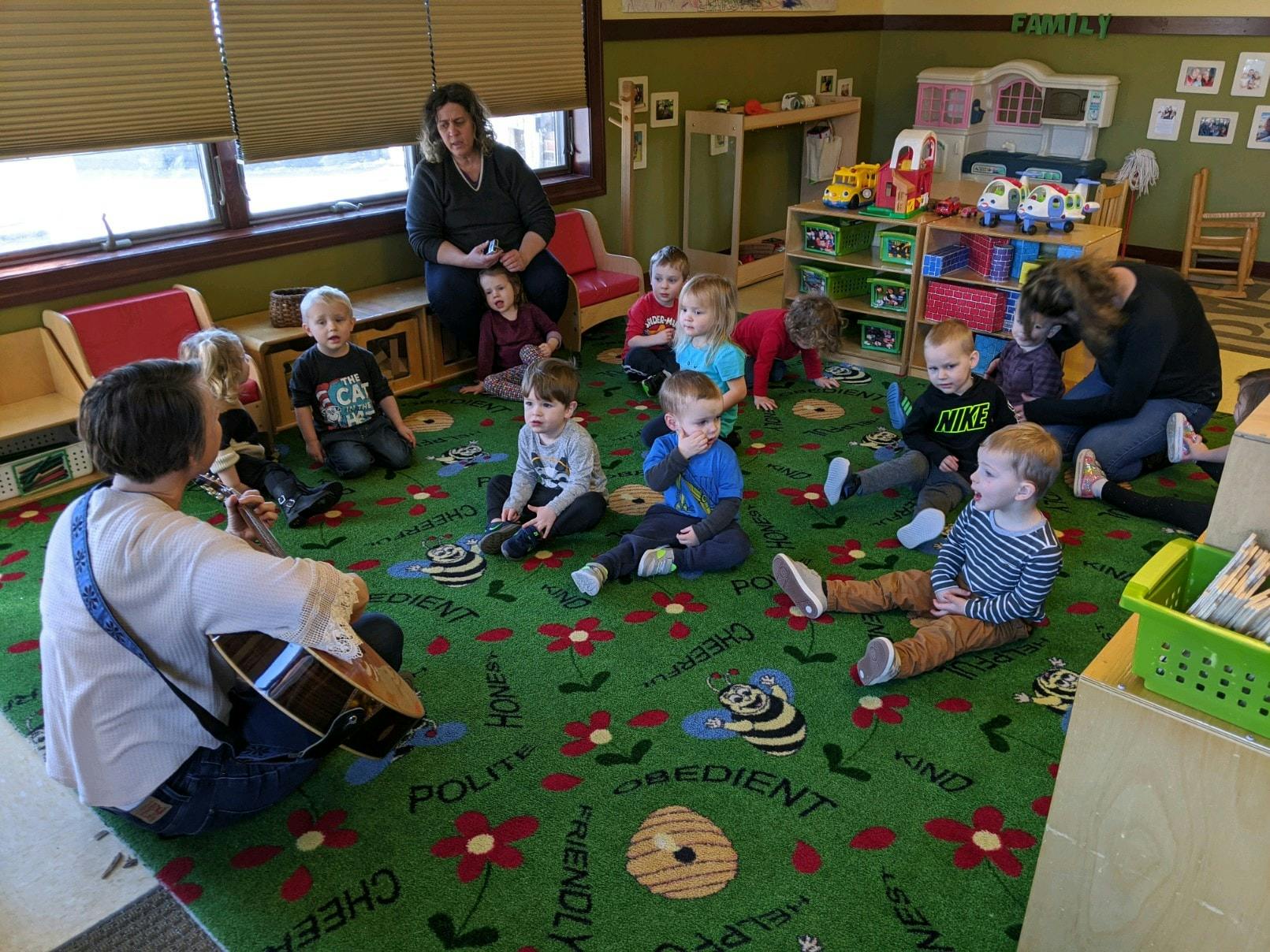 Person playing guitar for a group of children and adults in a classroom