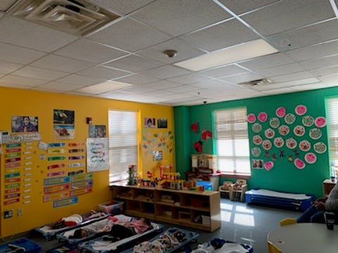 Classroom with yellow and green walls, windows, and cots on the floor