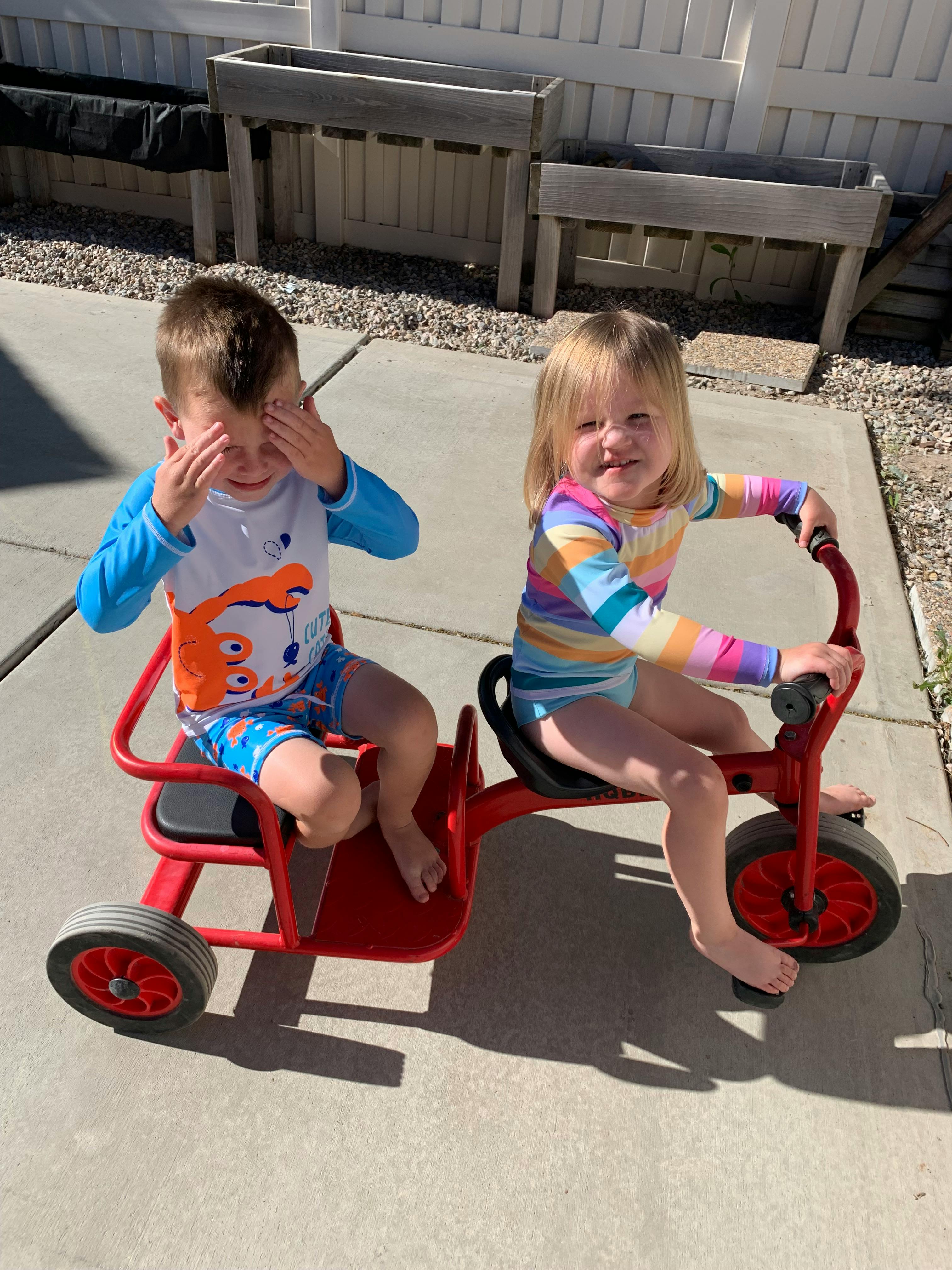 Two children on a red tandem tricycle