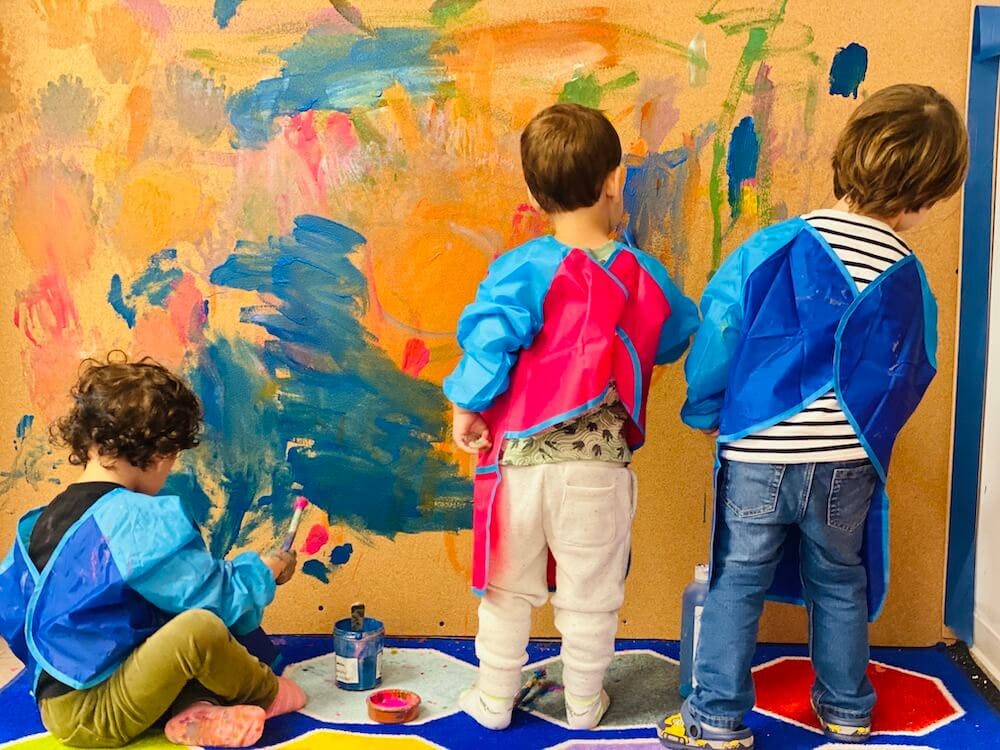 Three children painting on a large canvas