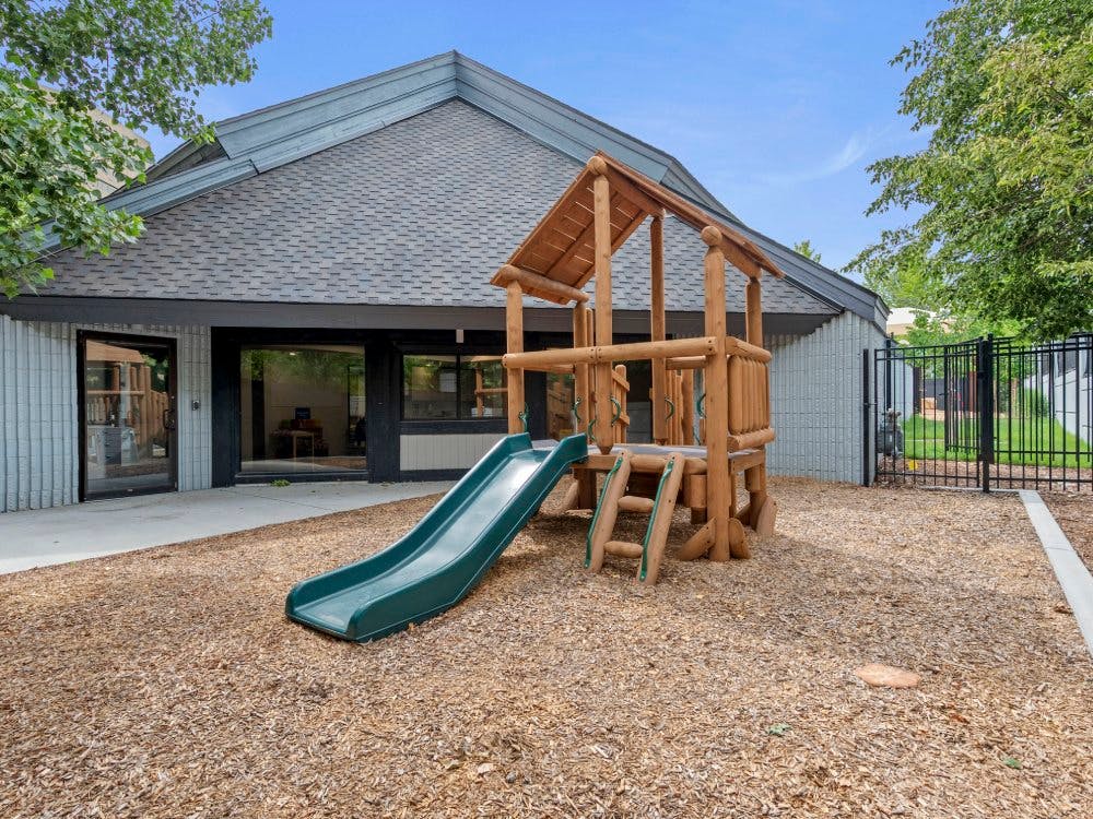 A wooden playground structure with a green slide outside a building