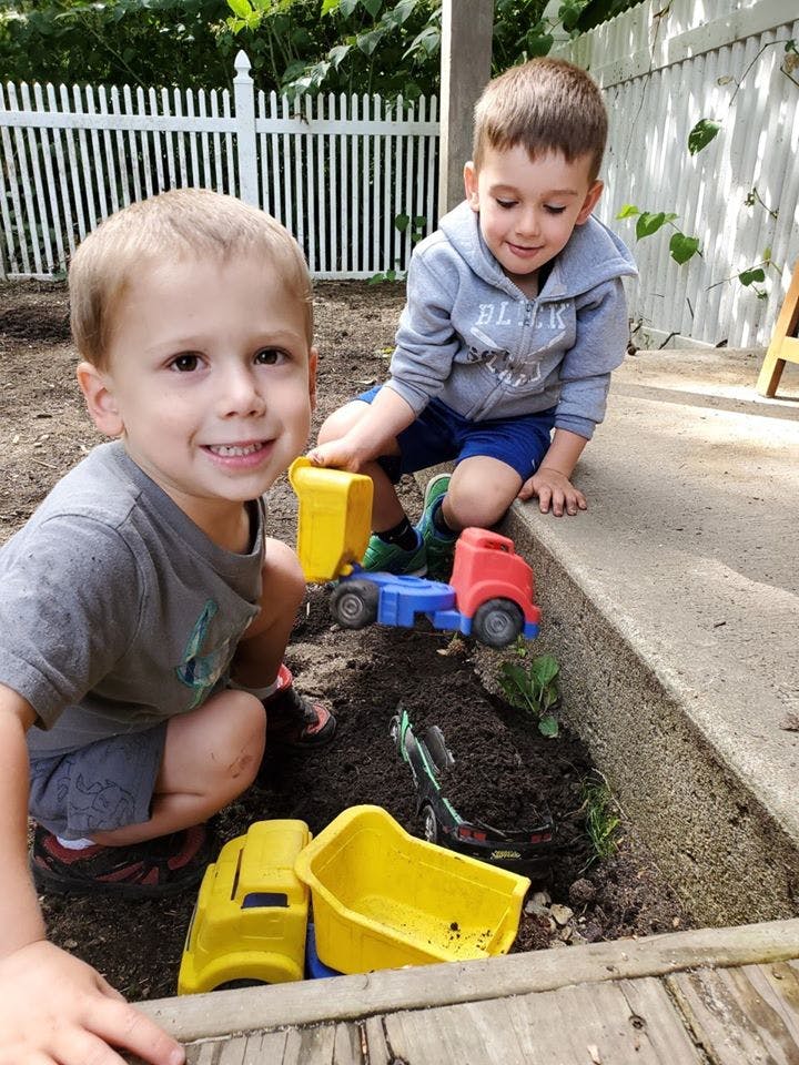 Two children playing with toy trucks in dirt