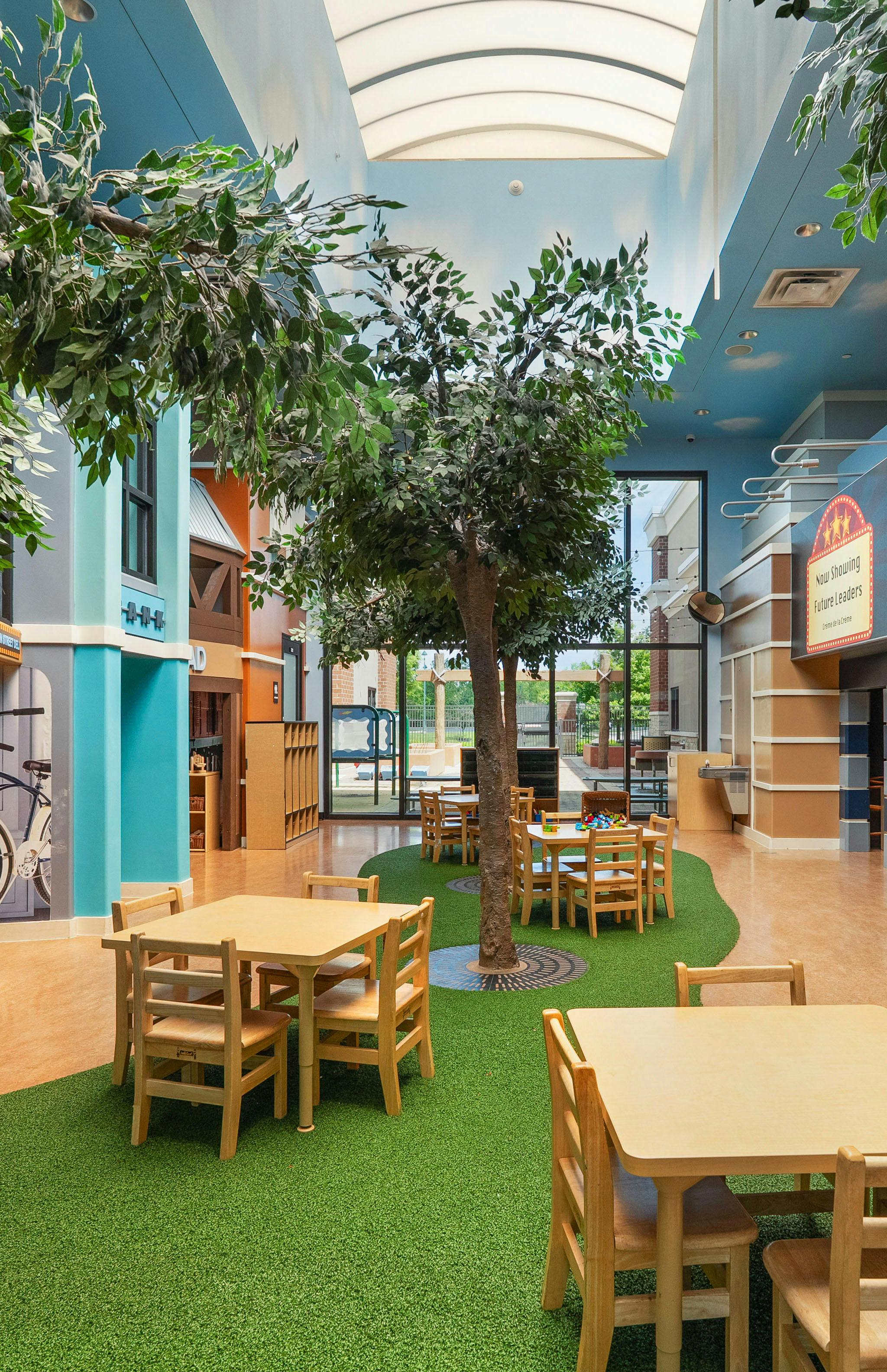 Classroom with small tables and chairs on artificial grass, trees inside