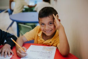 Child in a classroom writing on paper with a pencil