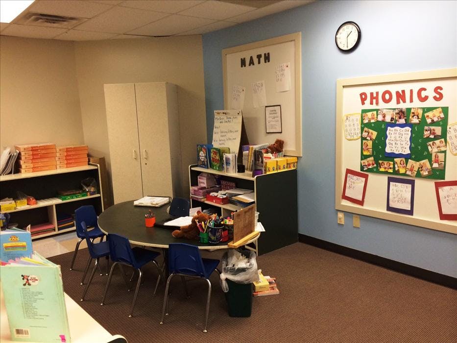A classroom with a round table and chairs, shelves, and boards labeled "MATH" and "PHONICS"