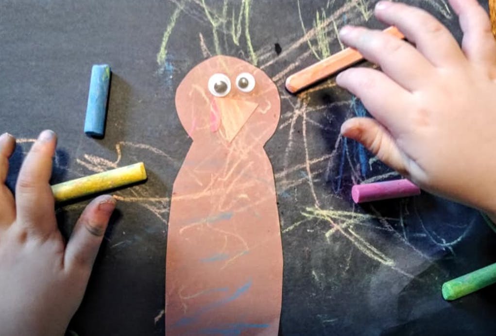 Child's hands drawing with chalk on a chalkboard next to a paper cutout