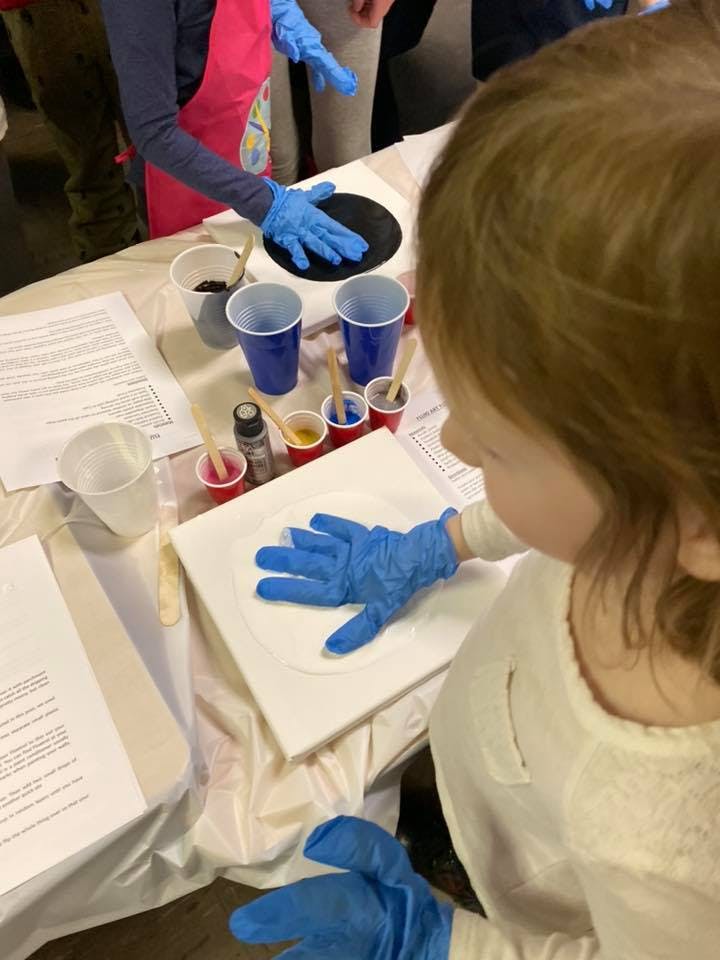 Child wearing blue gloves pressing hand onto white canvas