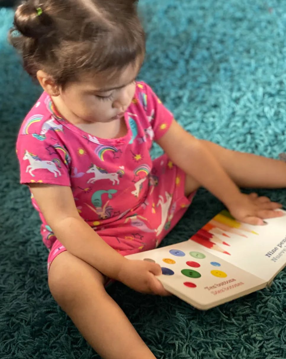 Child sitting on a rug, looking at an open book