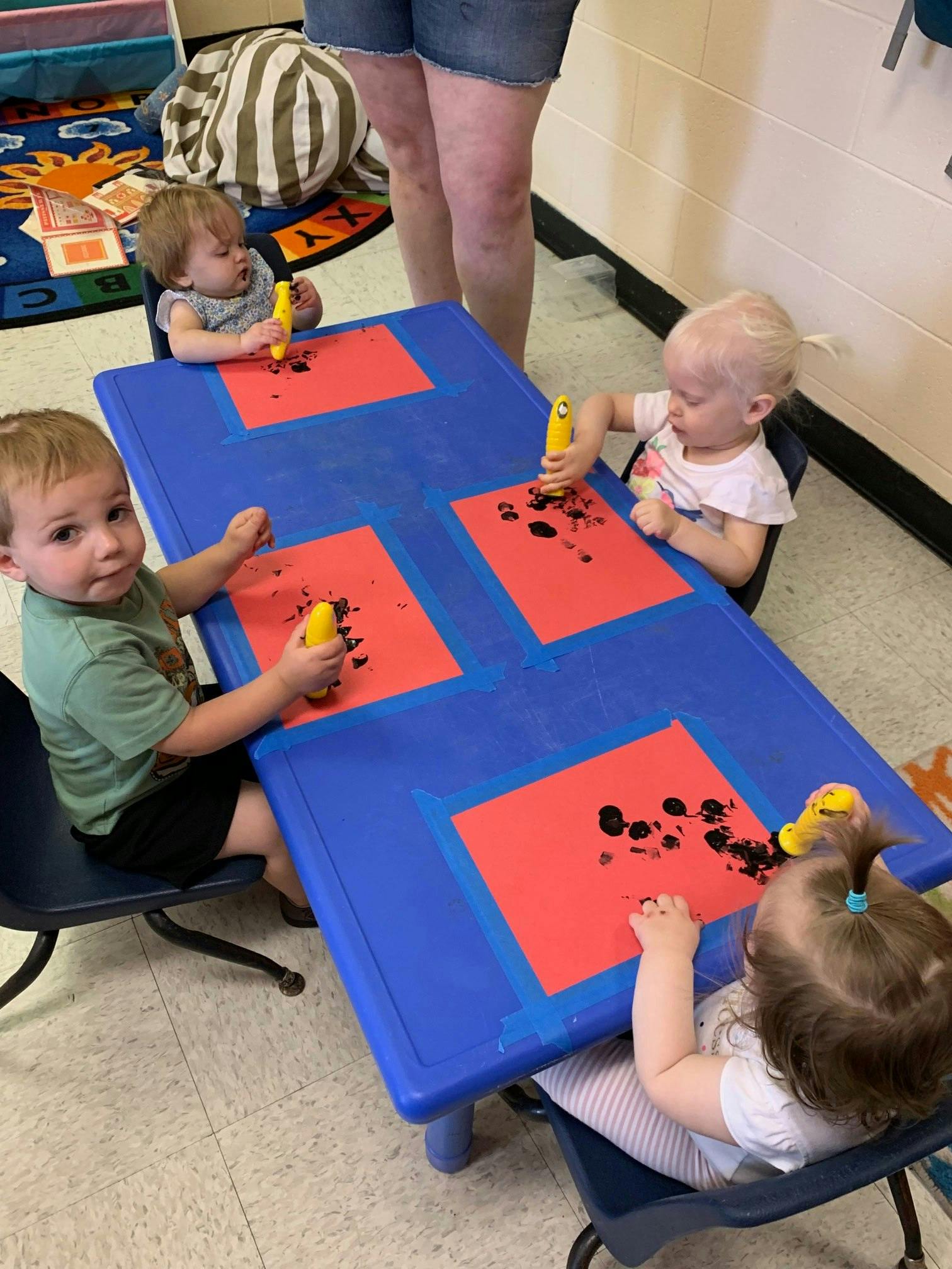 Four children painting at a blue table in a classroom