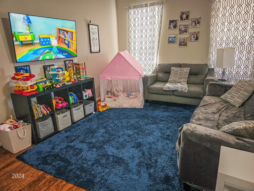 Living room with a large TV, toy storage, pink play tent, and two sofas