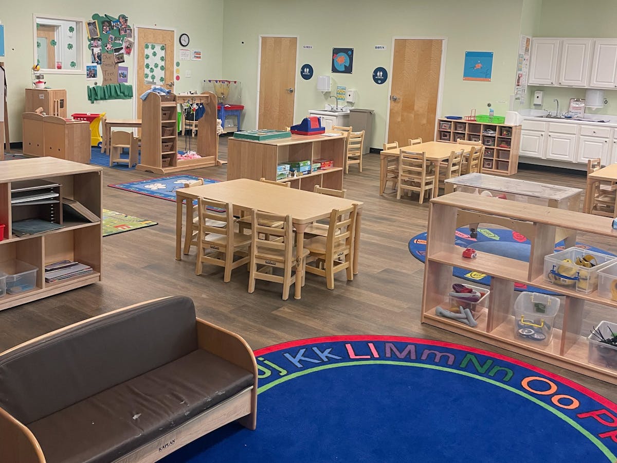 A classroom with small tables and chairs, shelves, and a sofa