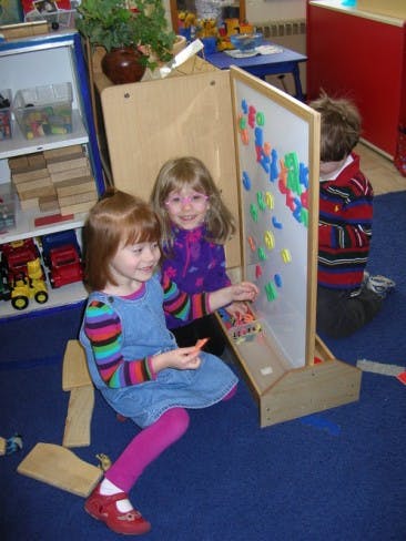 Two children playing with magnetic letters on an easel in a classroom