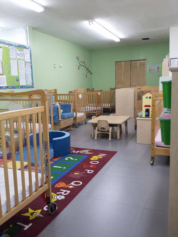 Nursery room with multiple wooden cribs, a small table and chairs, and an alphabet rug