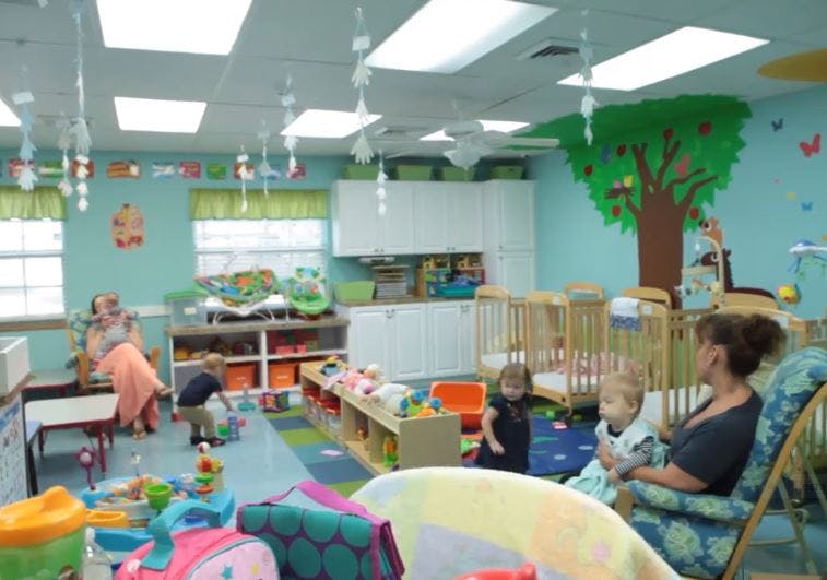 Adults and children in a brightly lit room with toys and cribs