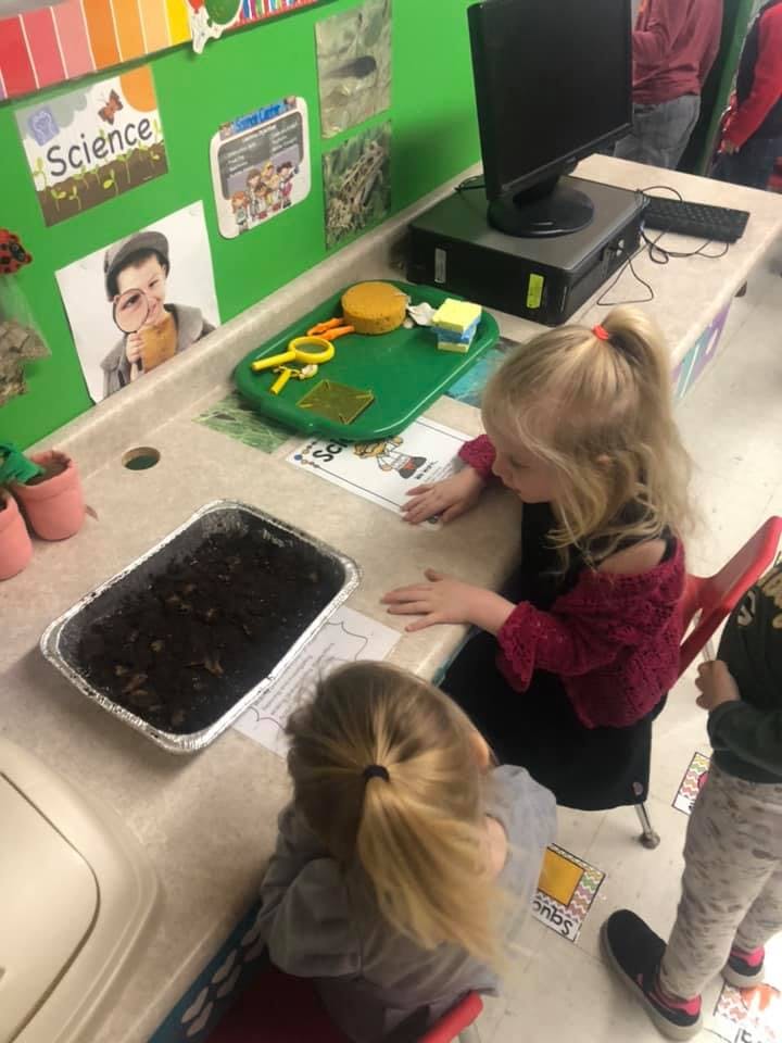 Two children at a table with a tray of soil and papers