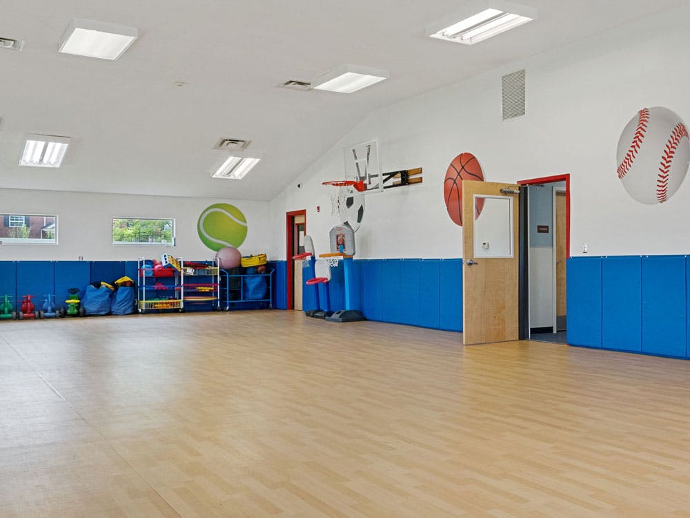Empty children's gymnasium with various sports equipment, toys, and large ball decals