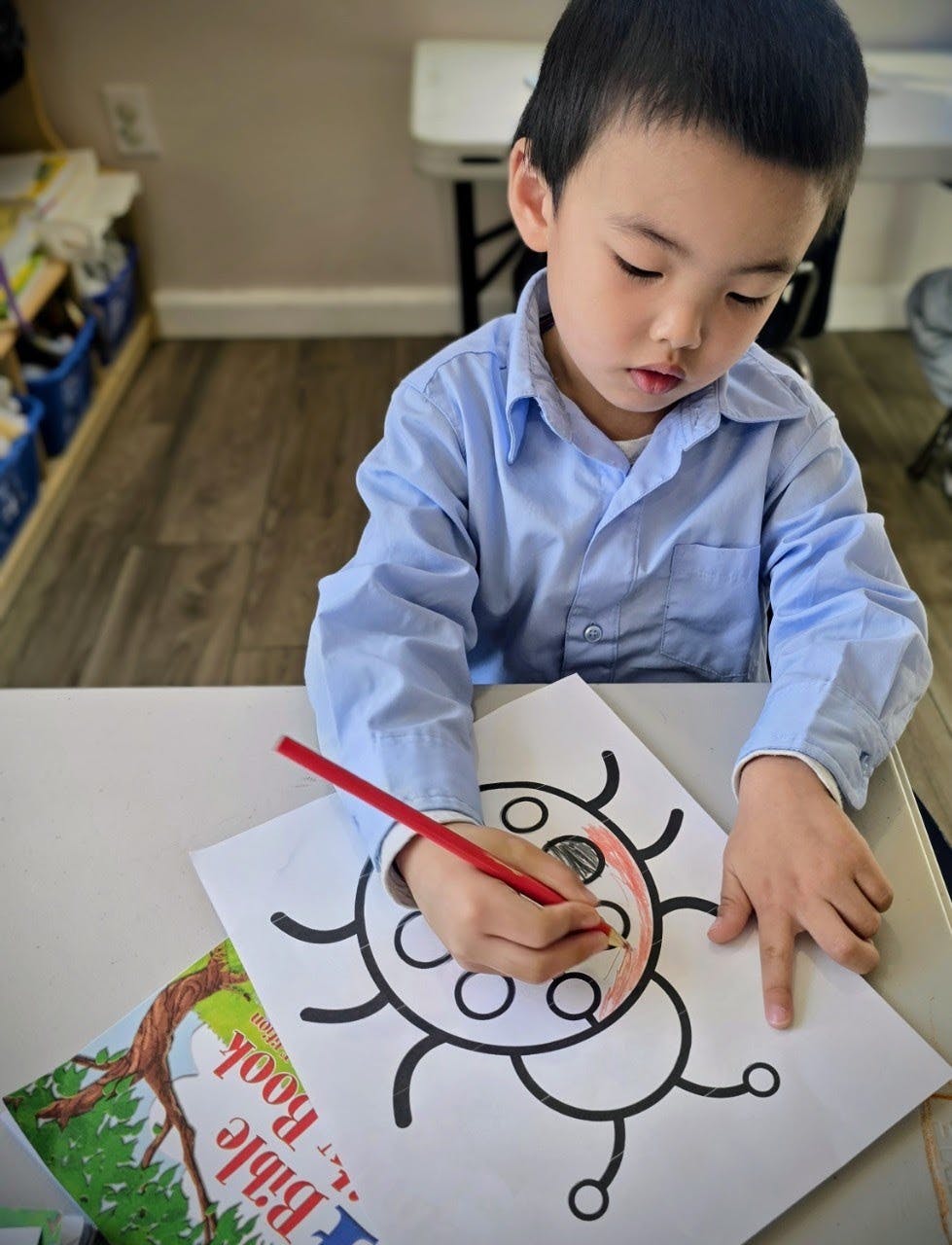 Child coloring a bug illustration on paper with a red pencil