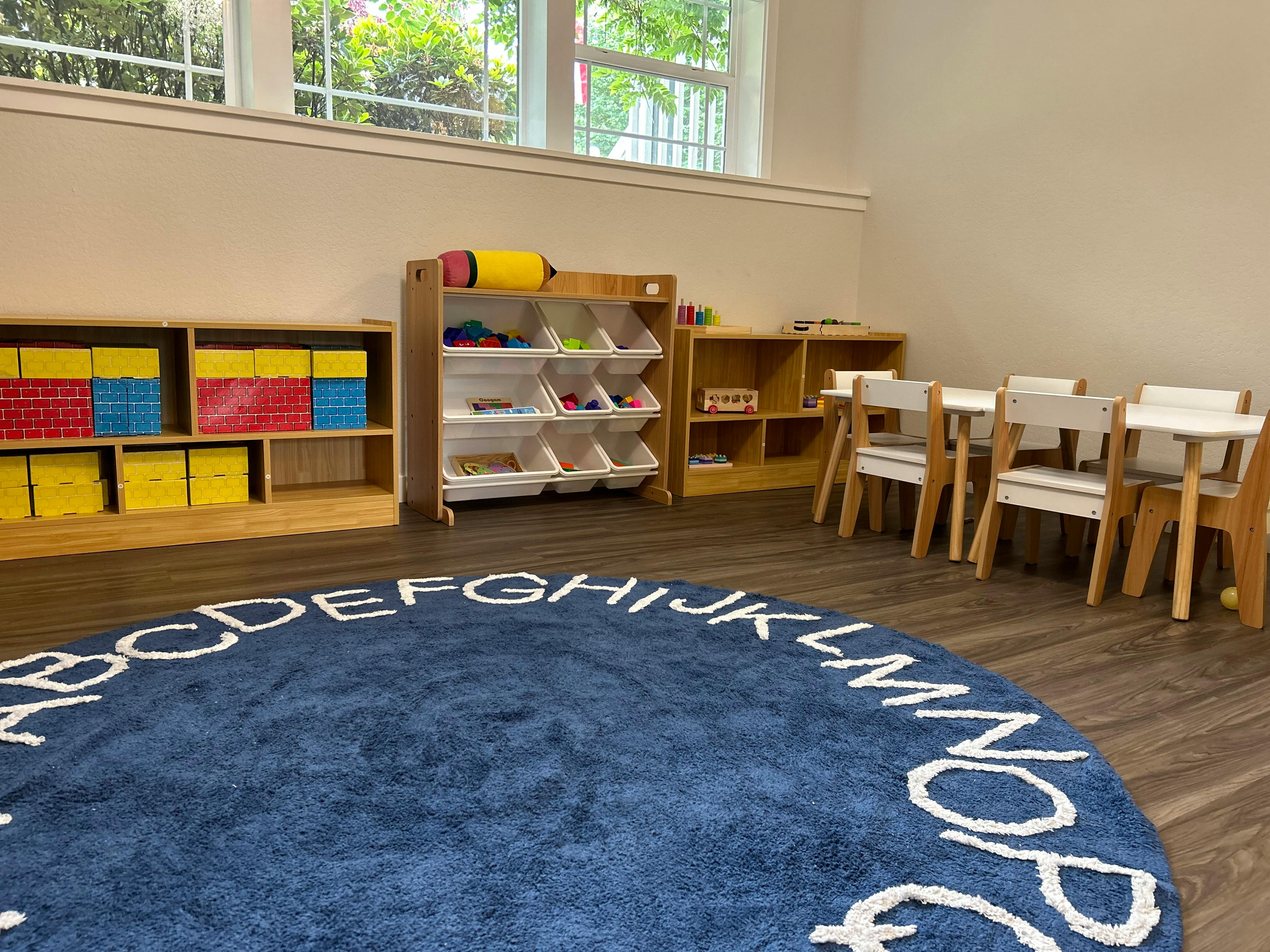 Classroom with an alphabet rug, storage shelves, and small tables with chairs