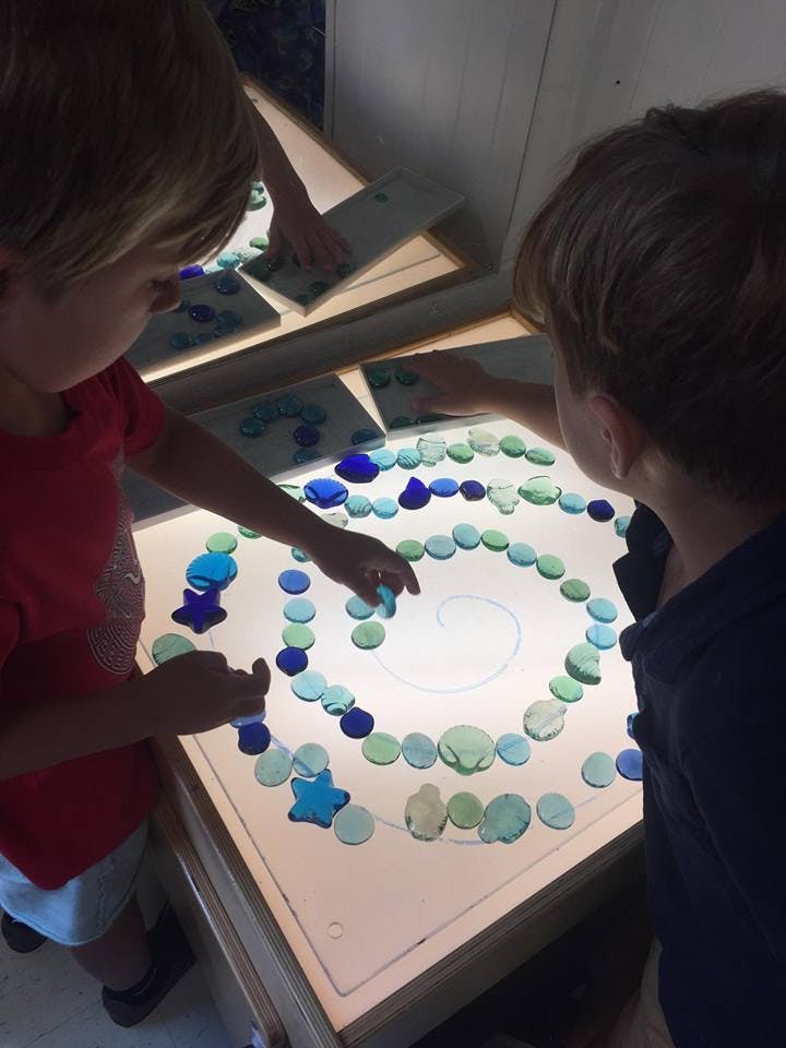 Two children arranging colorful translucent pieces on a light table