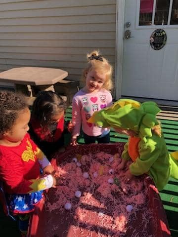 Three children playing with a sensory bin filled with pink material and white objects