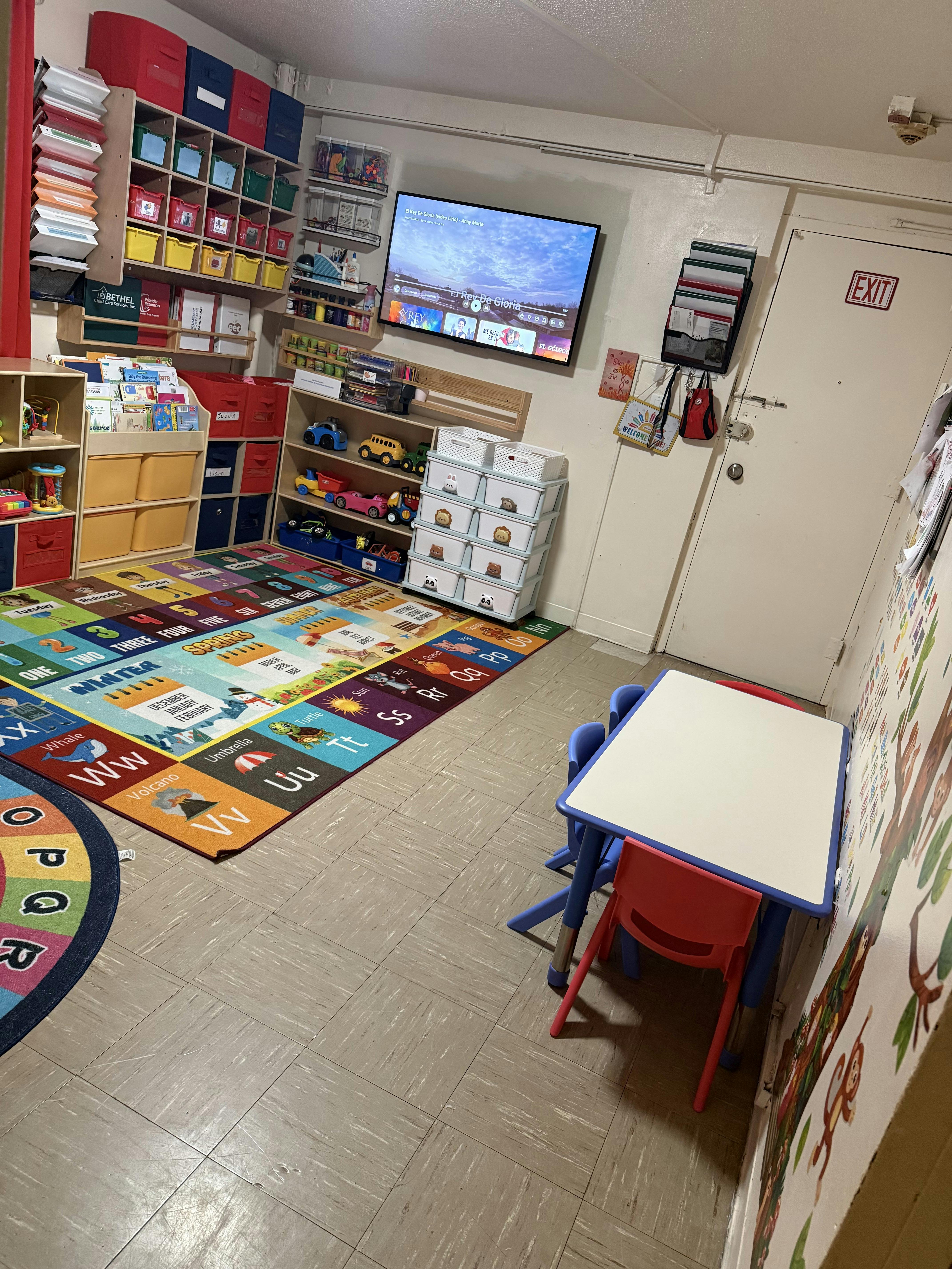 Children's playroom with colorful ABC rug, shelves of toys and books, and a small table with chairs