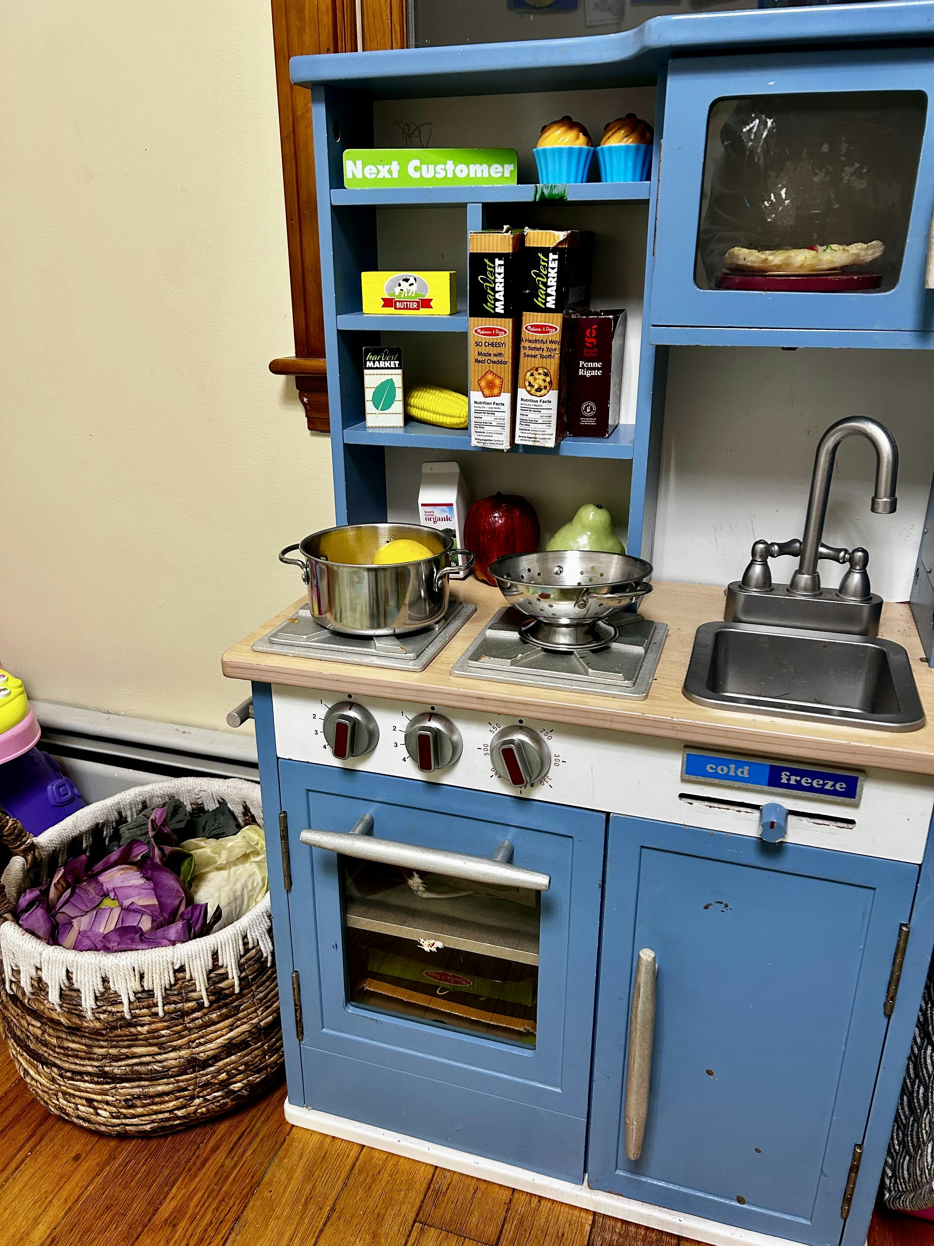 Child's play kitchen with blue cabinets, a sink, stove, and various play food items