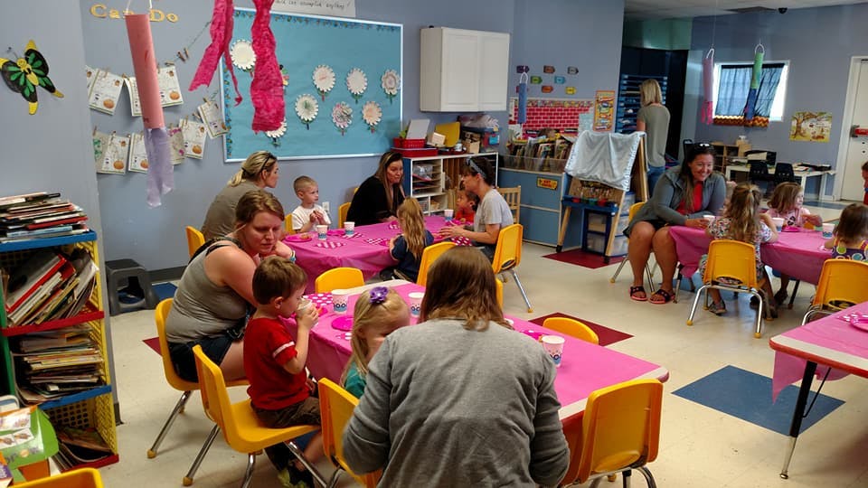 People and children sitting at tables in a classroom