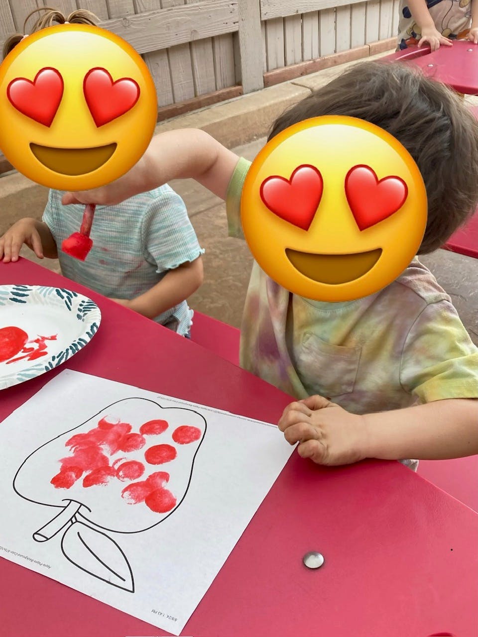 Child finger painting a red apple on a white paper