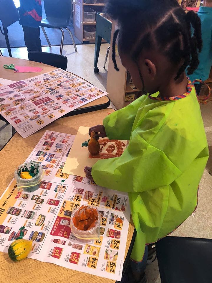 Child in a green smock working on a craft at a table
