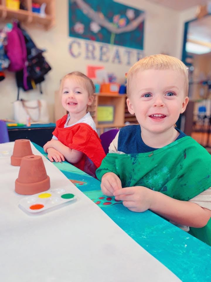 Two children at a table with paint and small terracotta pots