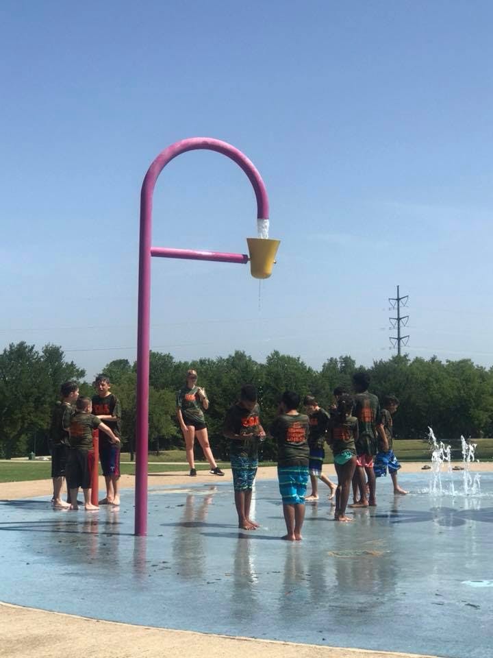 Children and adults playing in a splash pad with a large purple water feature