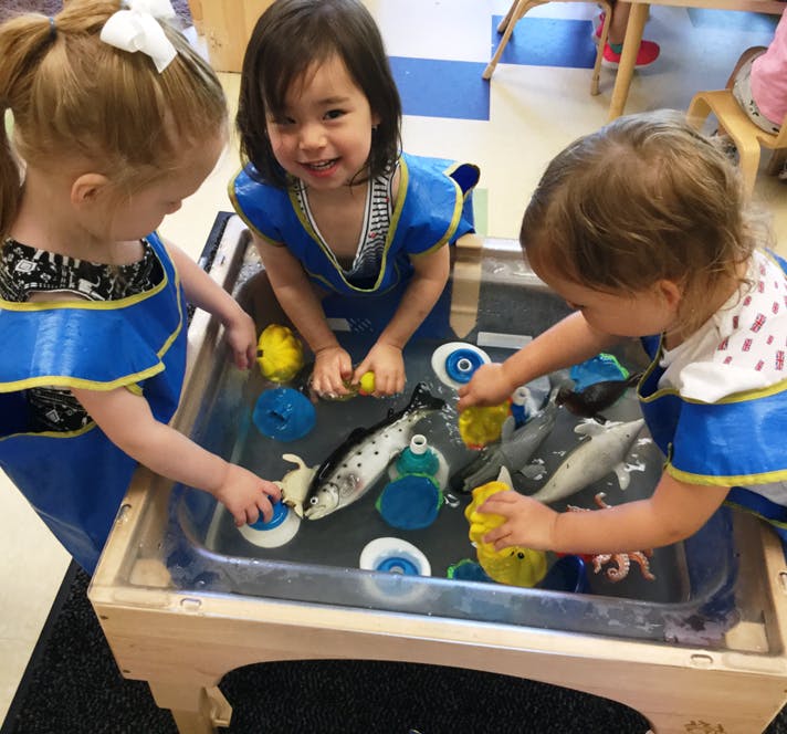 Three children playing with toys in a water table