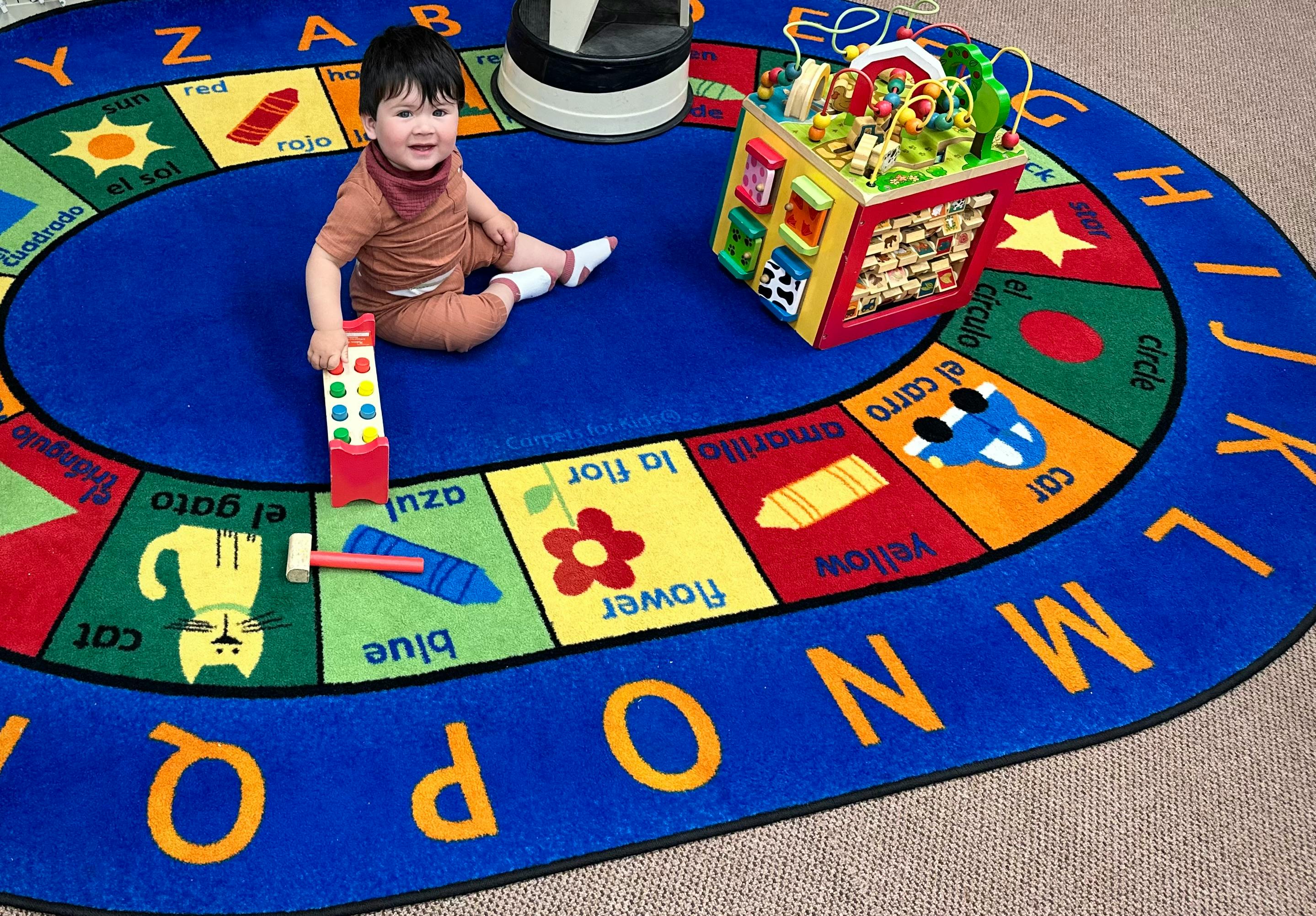 Child sitting on an alphabet rug with toys