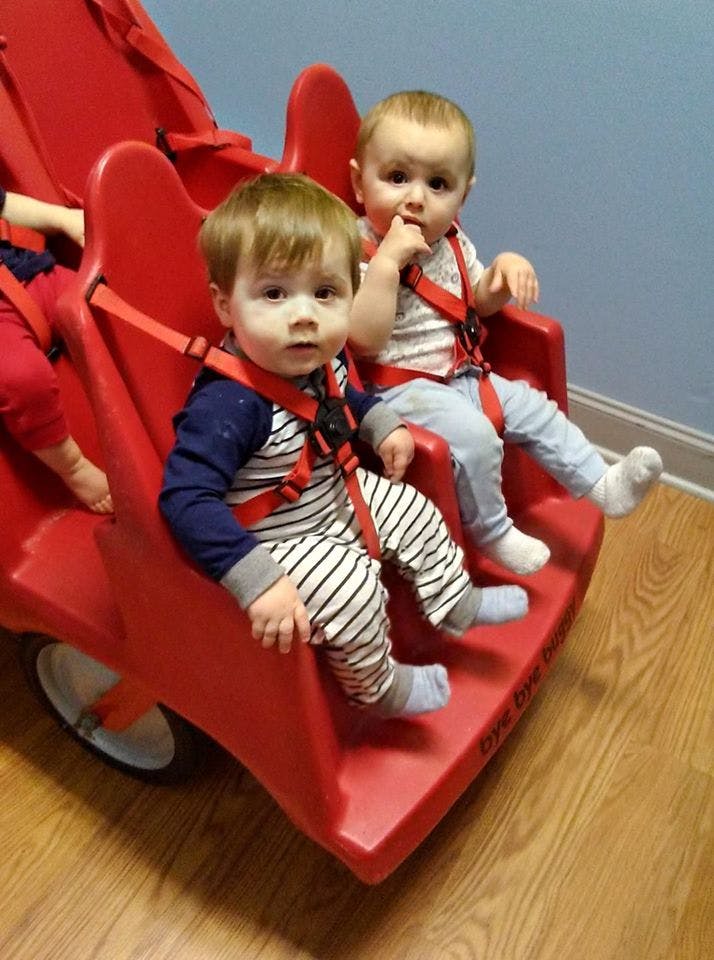 Two children sitting in a red multi-seat stroller