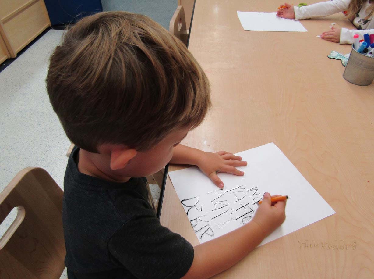 Child drawing on paper with an orange crayon