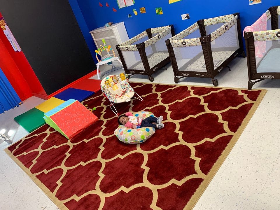 Child sleeping on a pillow on a rug in a room with cribs