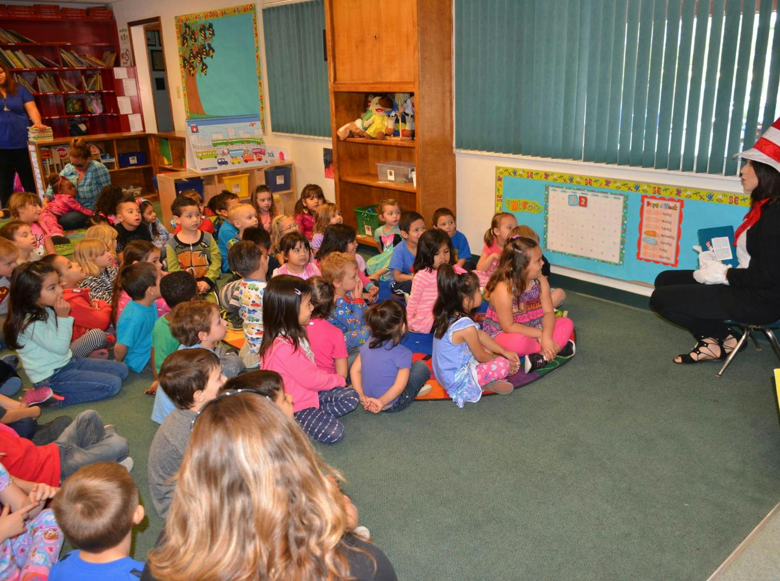 Person in striped hat reading to children in a classroom