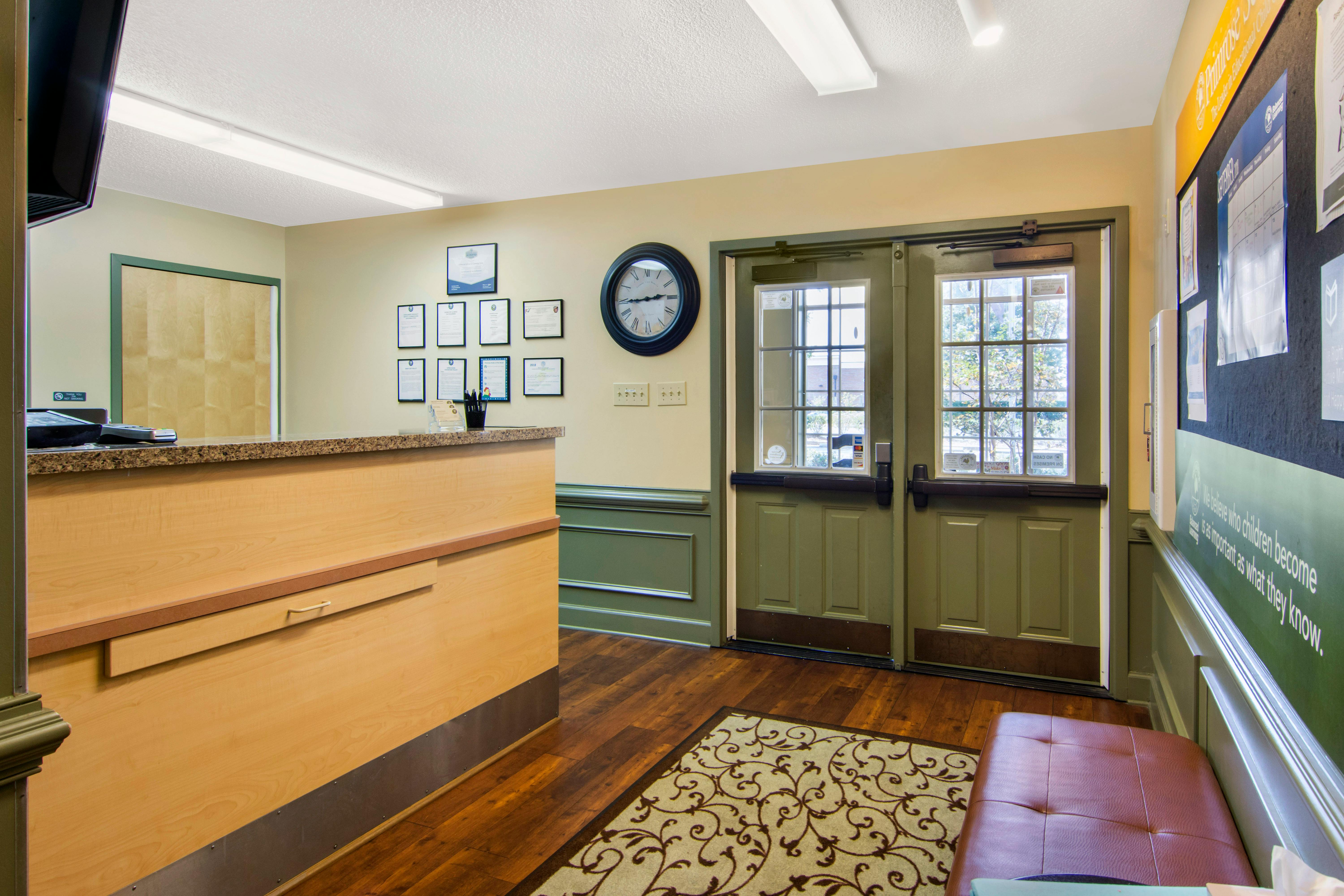 Reception area with a wooden desk, awards on the wall, and double doors