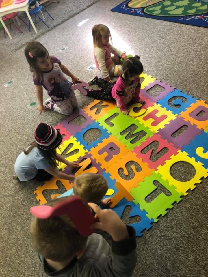 Children playing with colorful alphabet puzzle mats on the floor