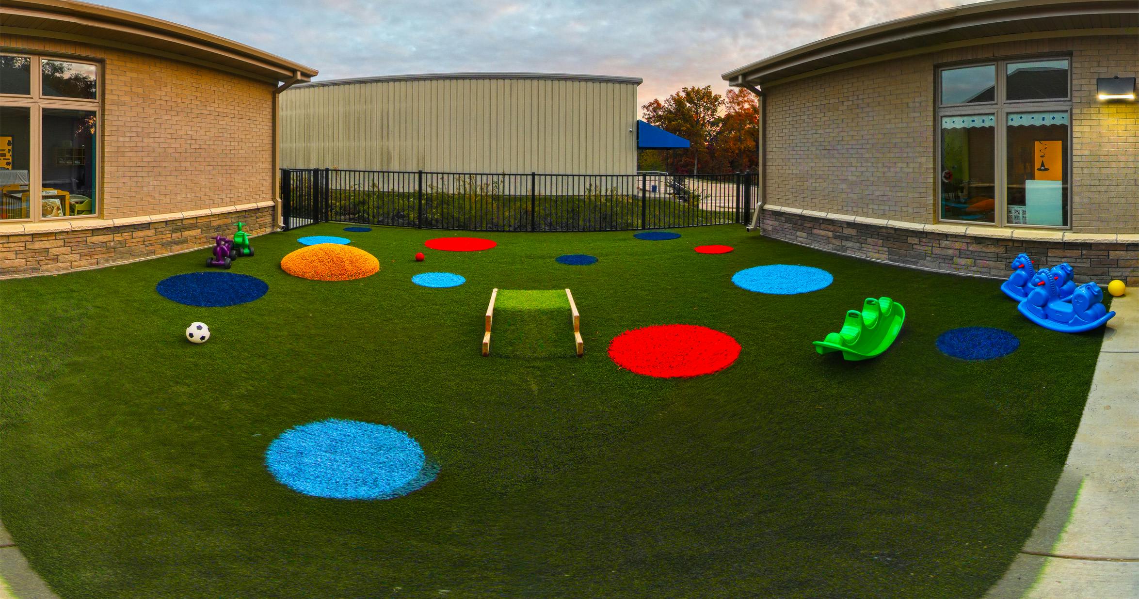 Outdoor play area with green turf, colorful circles, and rocking toys