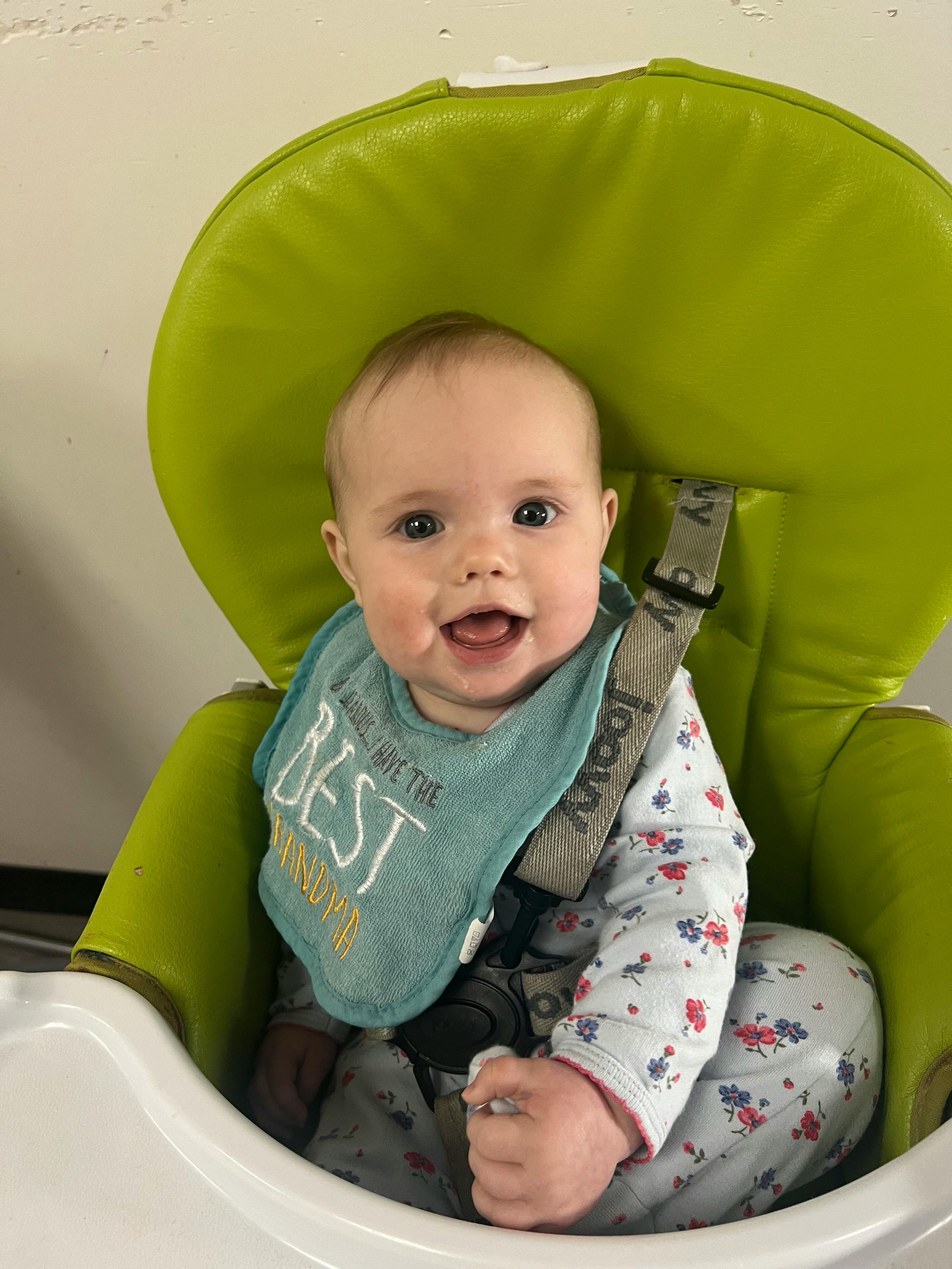 Child in a high chair wearing a bib that says "BEST"