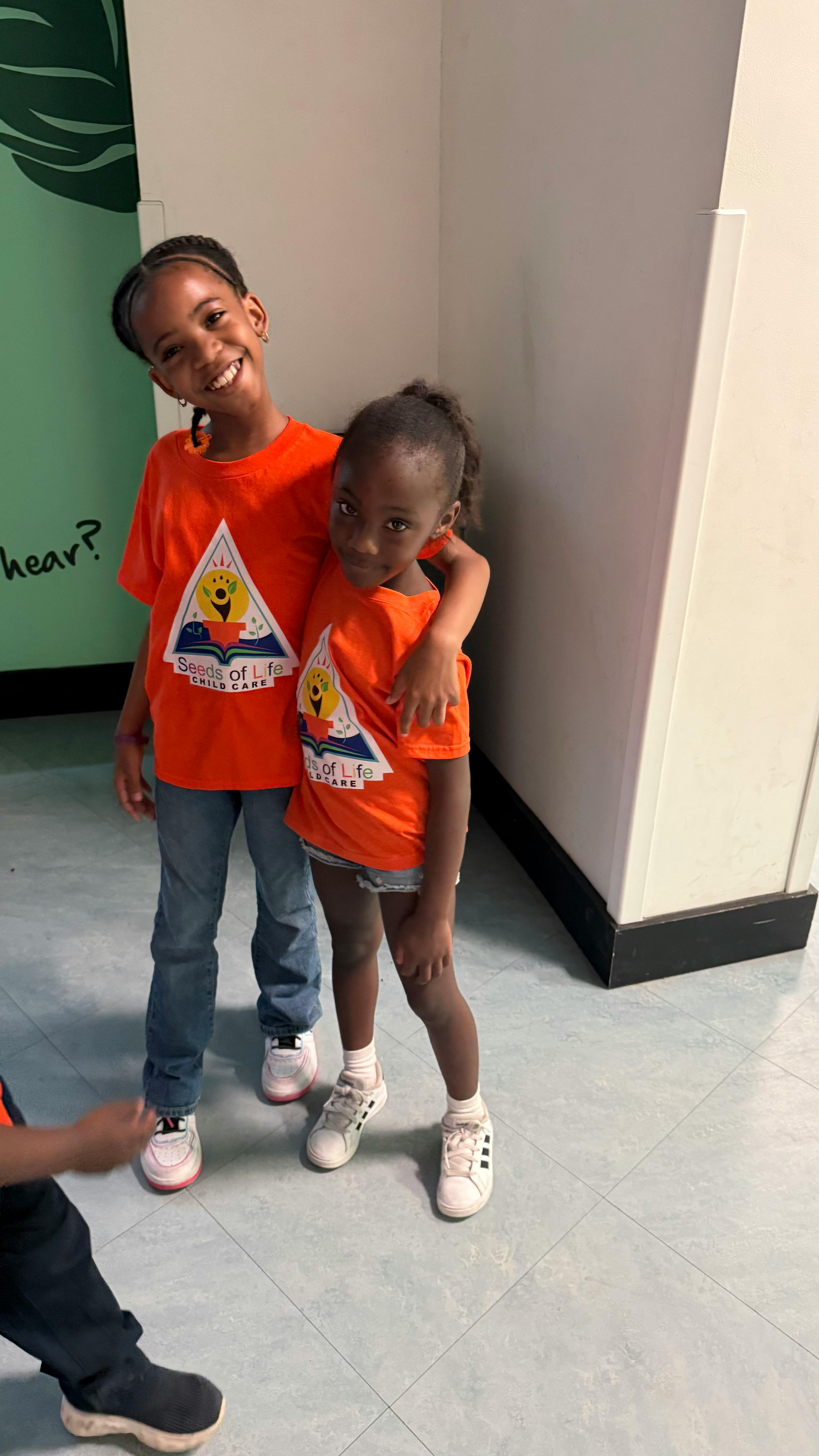 Two children wearing matching Seeds of Life Child Care orange t-shirts