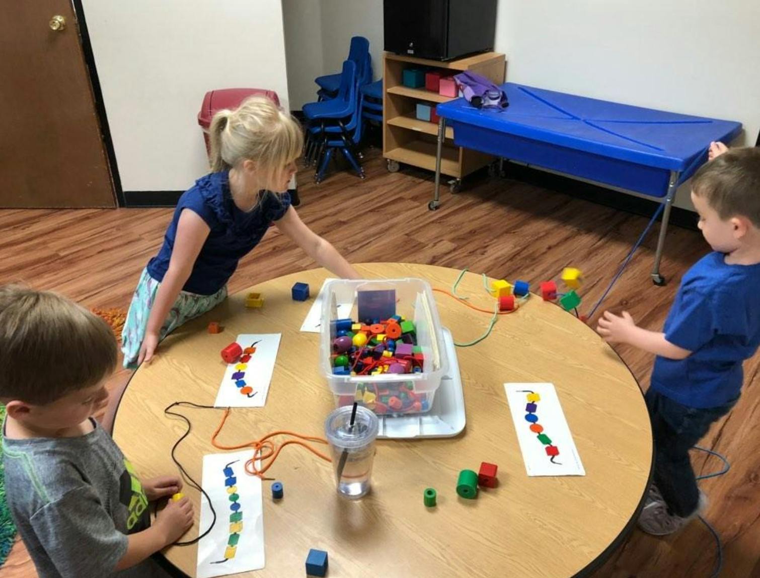 Three children playing with colorful blocks at a round table