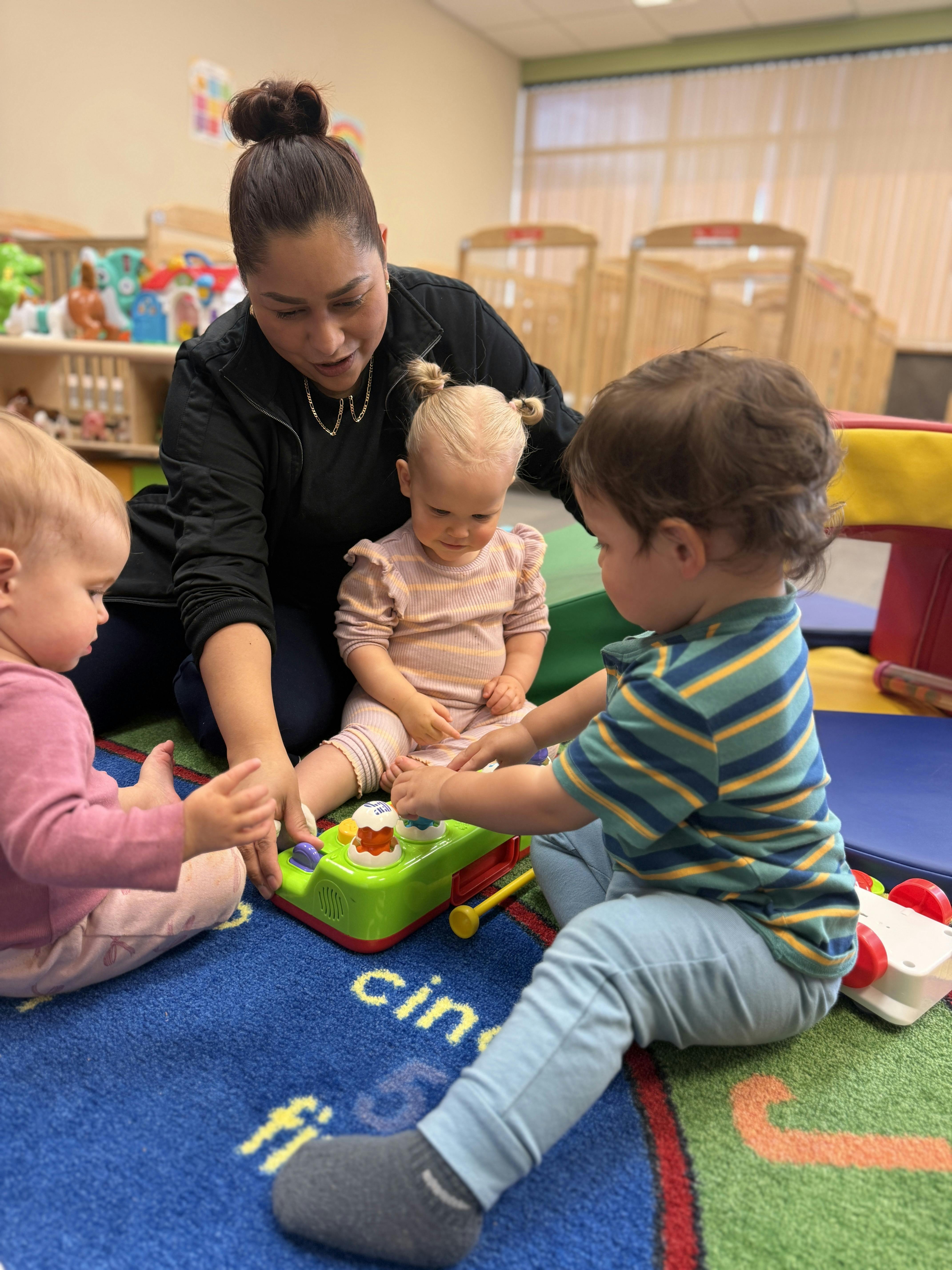 Adult and three children on a rug playing with toys in a classroom