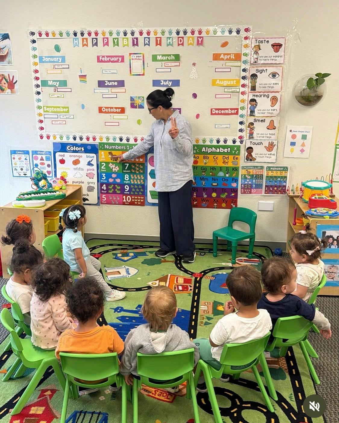 Teacher pointing to a numbers chart while children sit in a circle on a rug