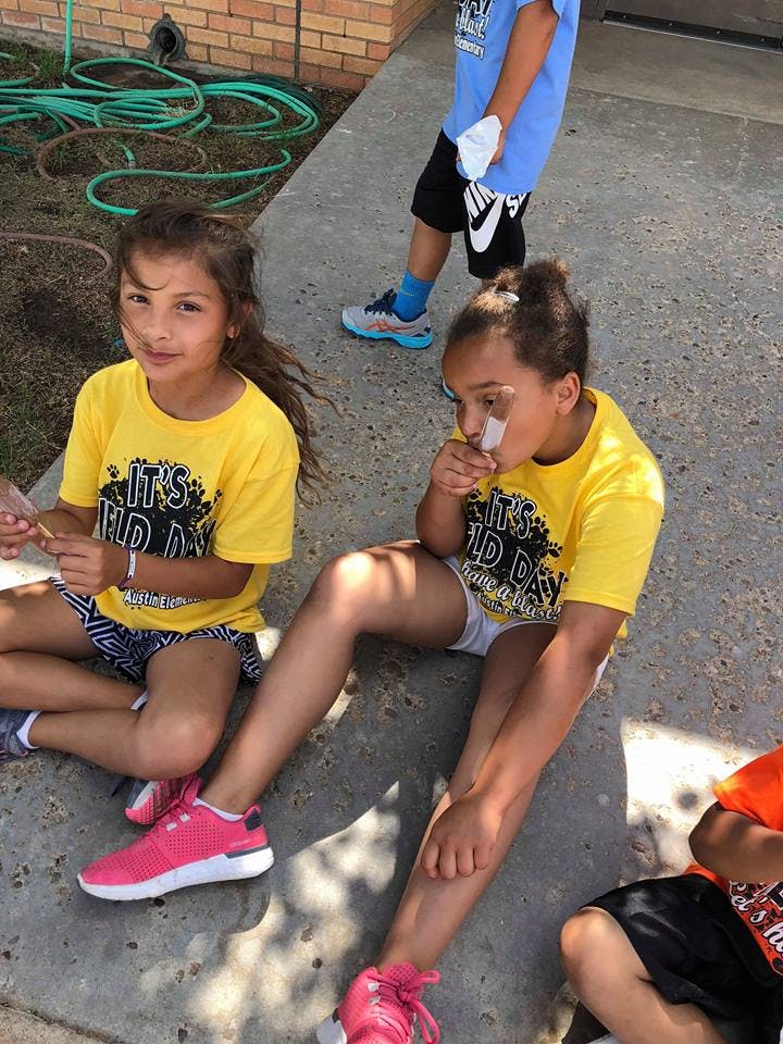 Two children sitting on the ground, one looking forward and one eating