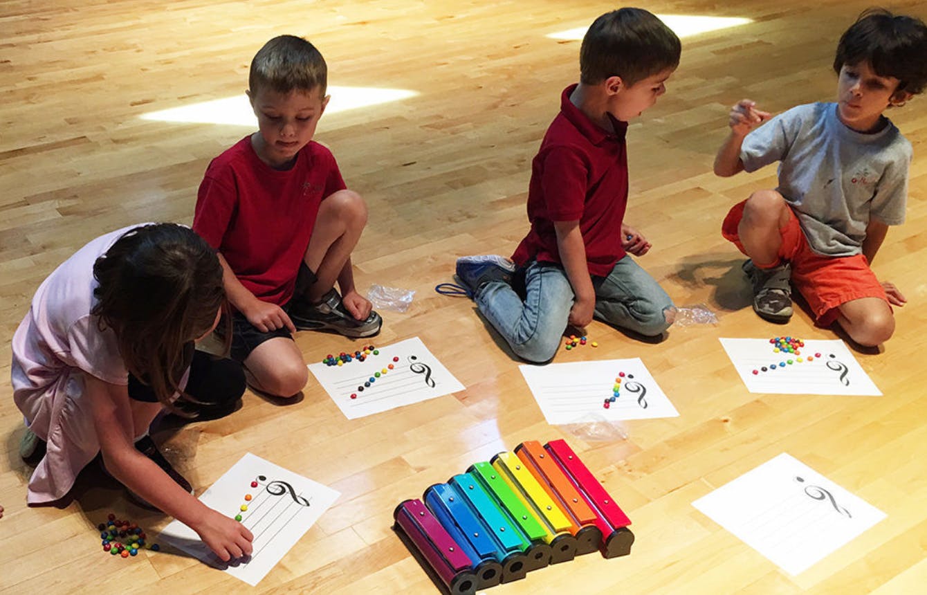 Children on floor with papers and colorful xylophone