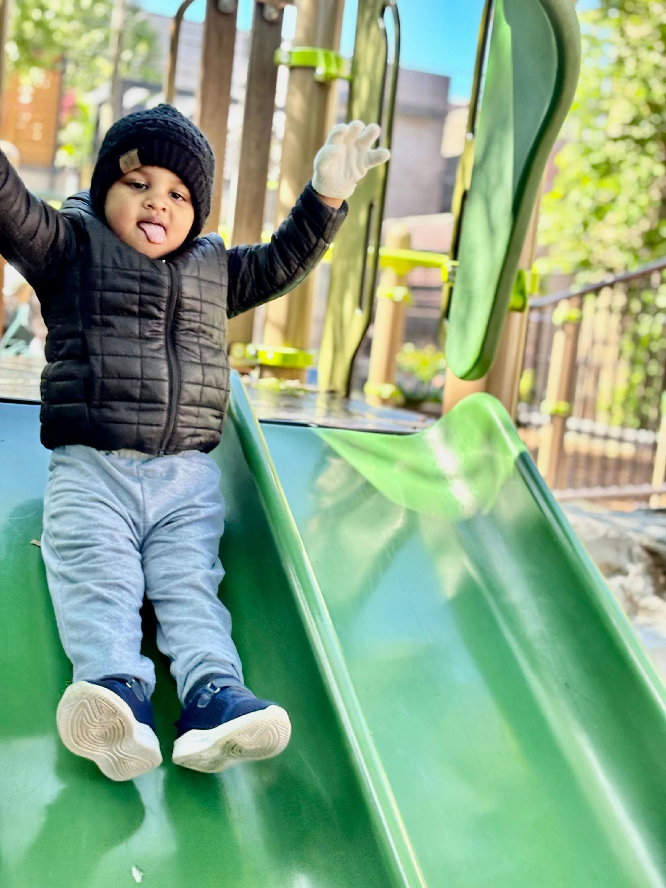 Child on a green slide with arms raised