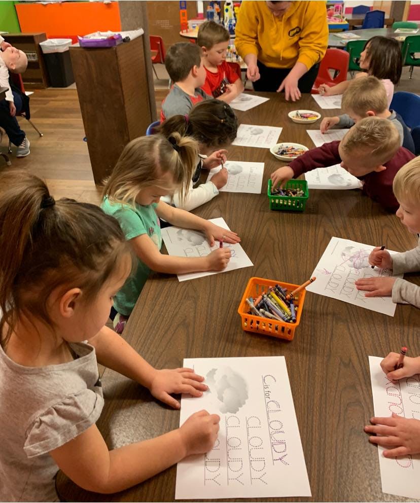Children drawing at a table with an adult supervising