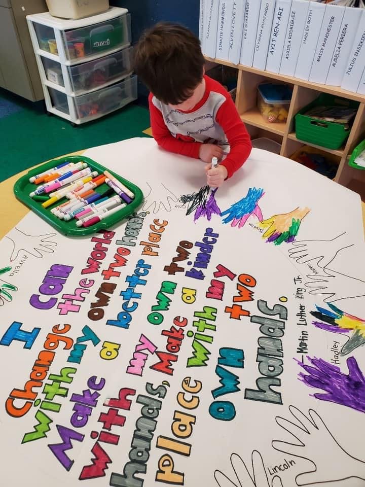 Child coloring a large paper with text "I can change the world with my own two hands"